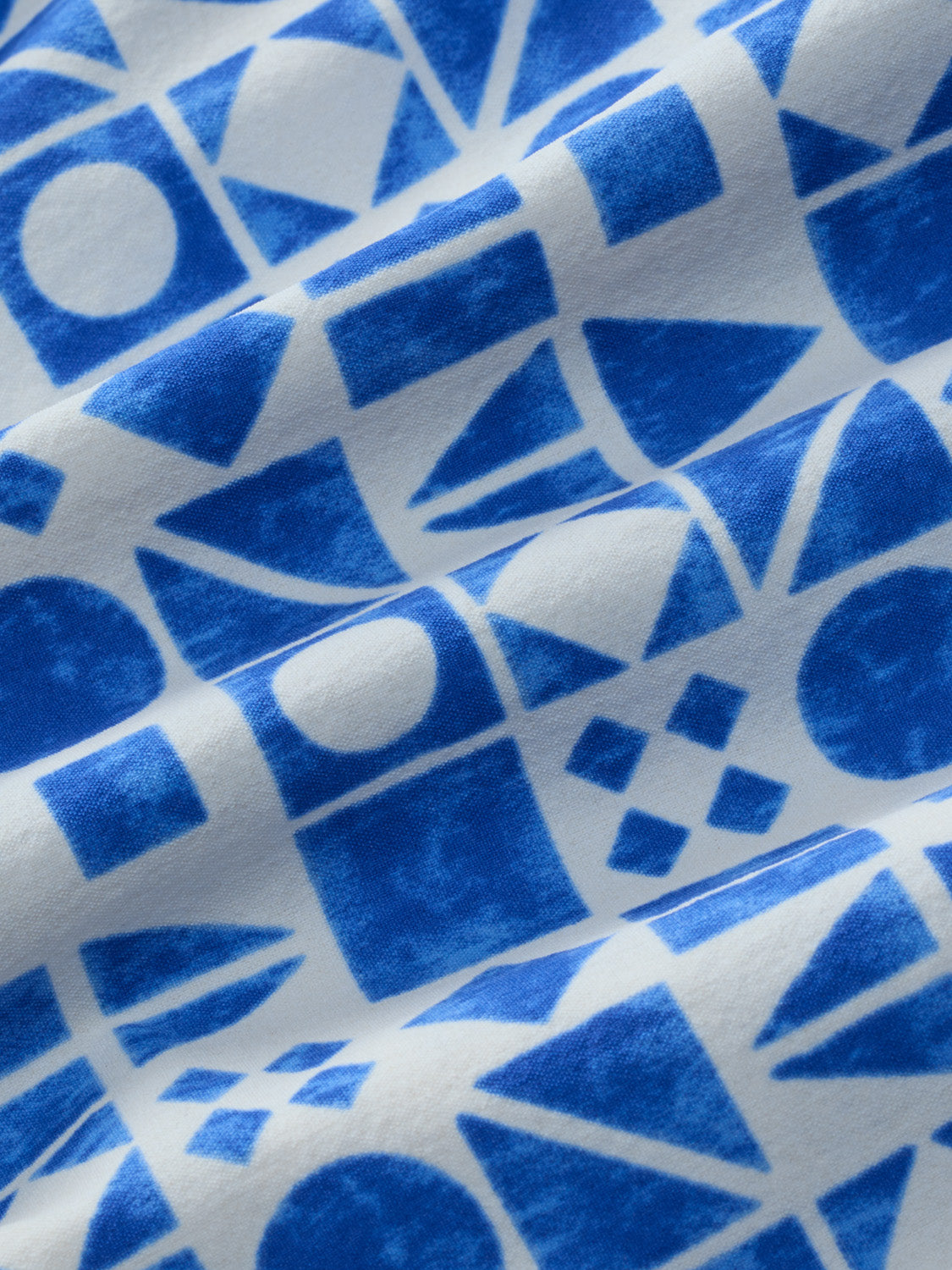 Blue and white geometric patterned fabric with triangles, circles, and rectangles throughout.