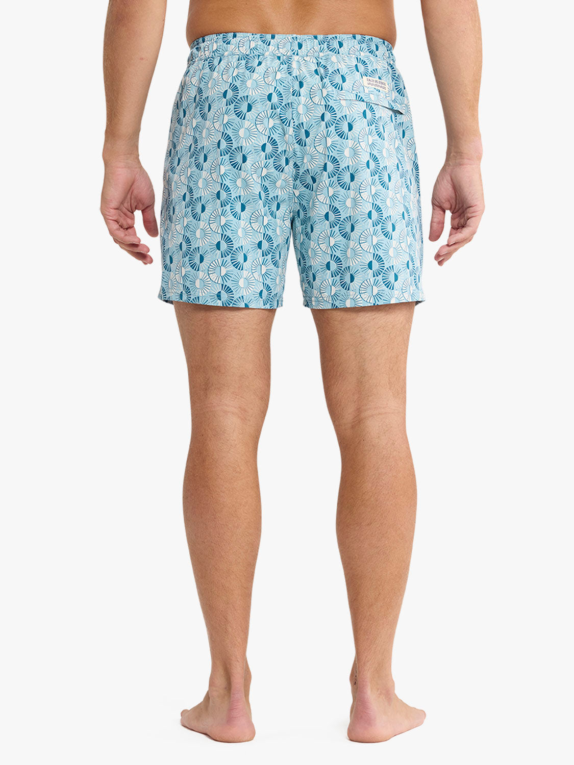 Man wearing light blue swim shorts with an all-over dark blue sunburst leaf pattern design.