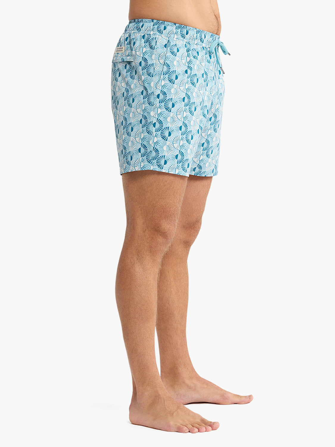 Man wearing bay blue swim trunk with sunburst palm leaf print and drawstring waistband.