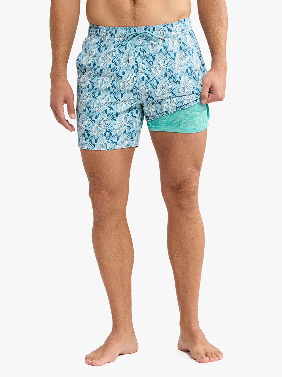 Man wearing blue sunburst patterned swim trunks with turquoise underside liner visible.