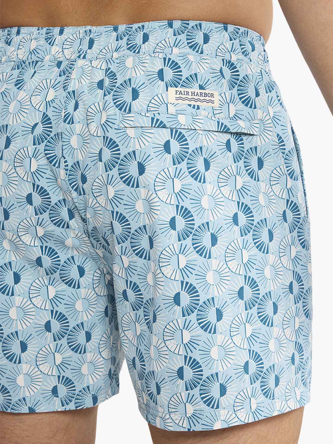 Light blue swim trunks with an all-over sunburst pattern in multiple shades of blue.