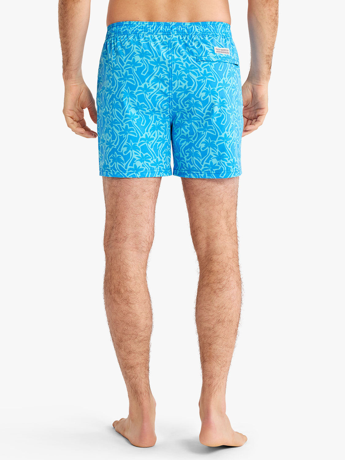 Man wearing turquoise swim trunks with light blue palm leaf cutout pattern throughout.