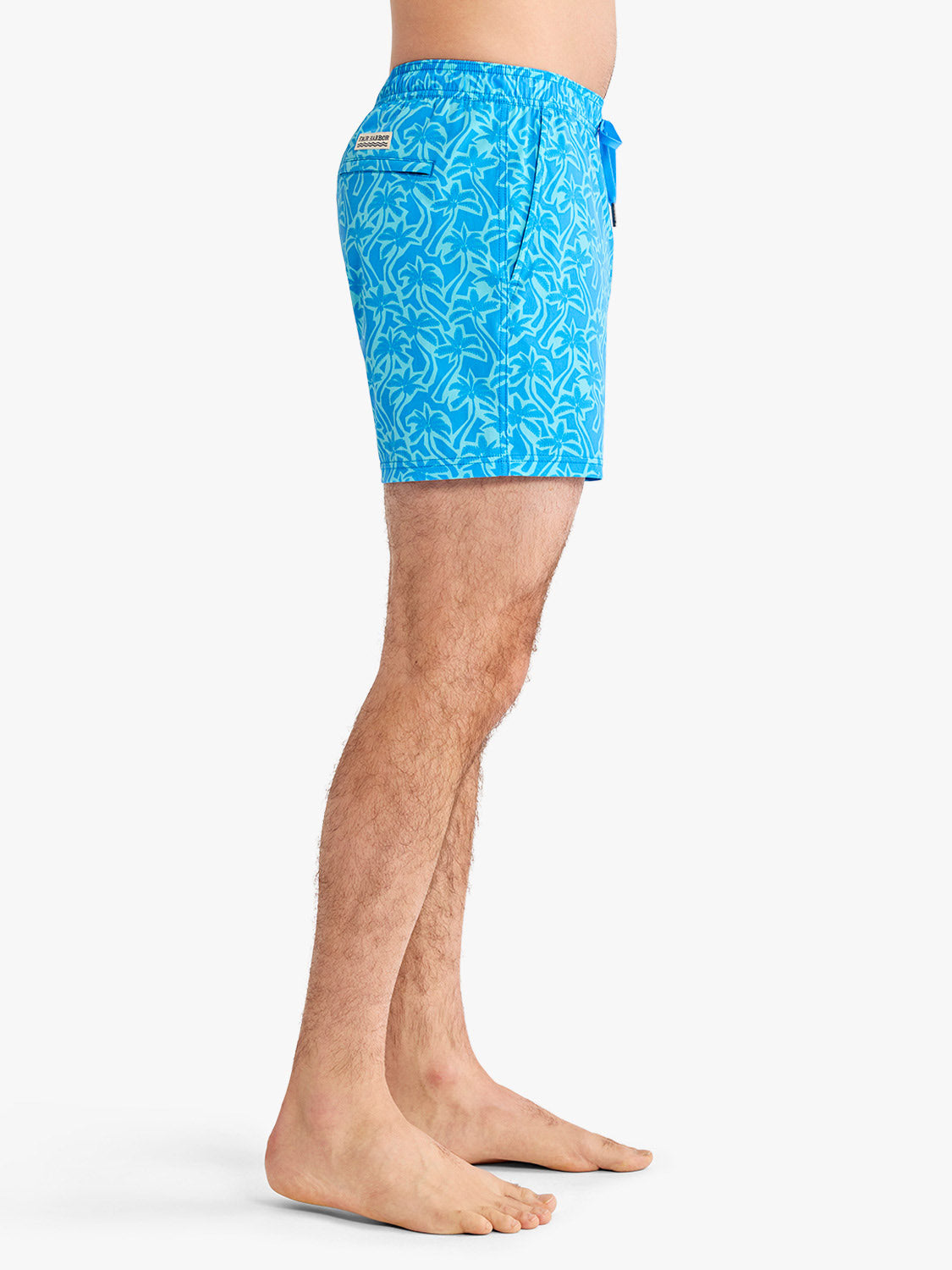 Turquoise swim trunk with pale palm leaf cutout pattern displayed on a man from waist down.