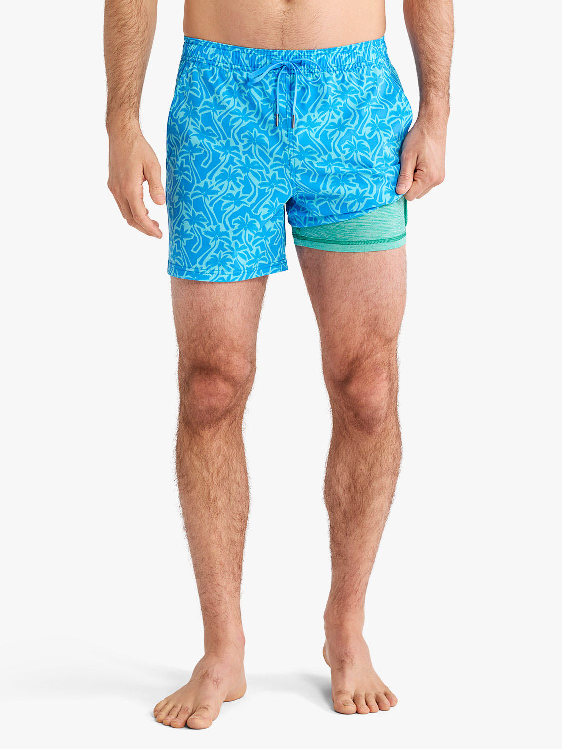 Man wearing turquoise swim trunks with cutout palm leaf pattern and green mesh side panel.