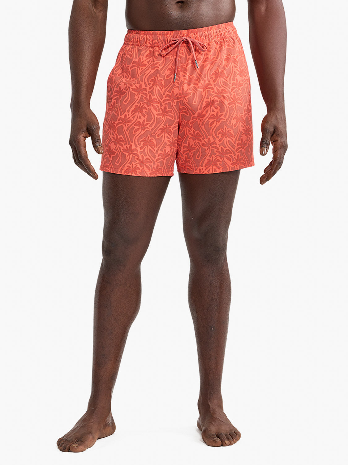 Man wearing coral swim trunks with cutout palm leaf pattern and drawstring waist.