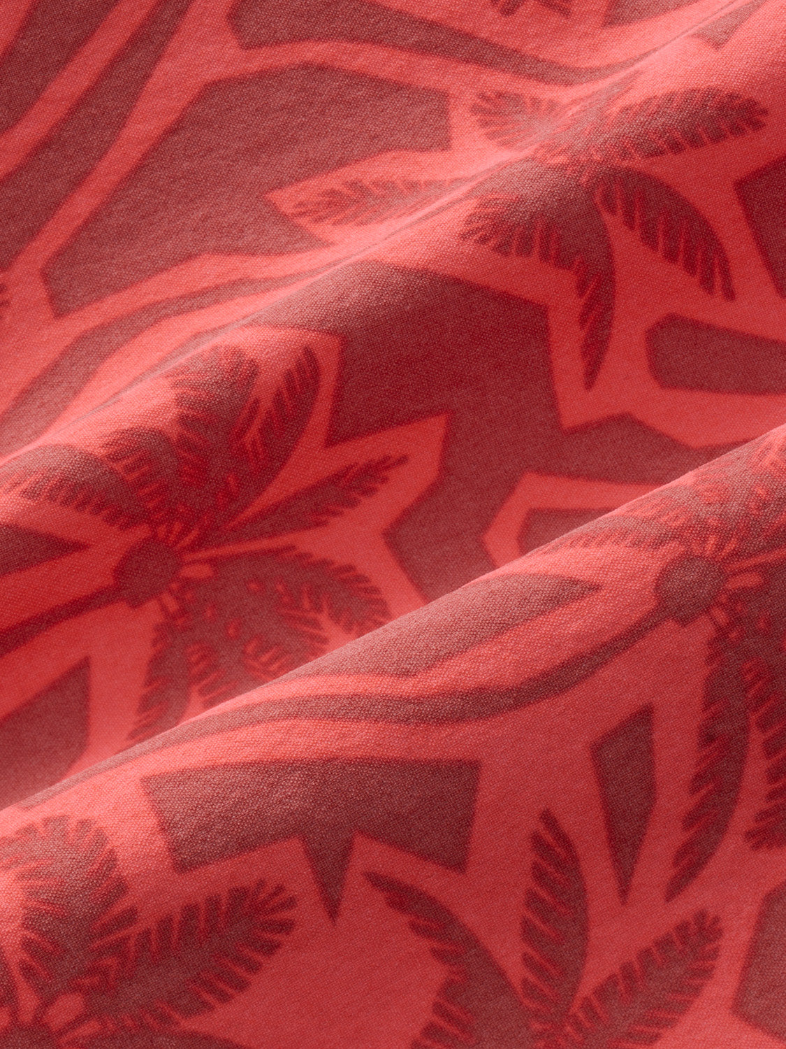 Coral fabric with a tonal cutout palm leaf pattern creating shadow effects across the surface.