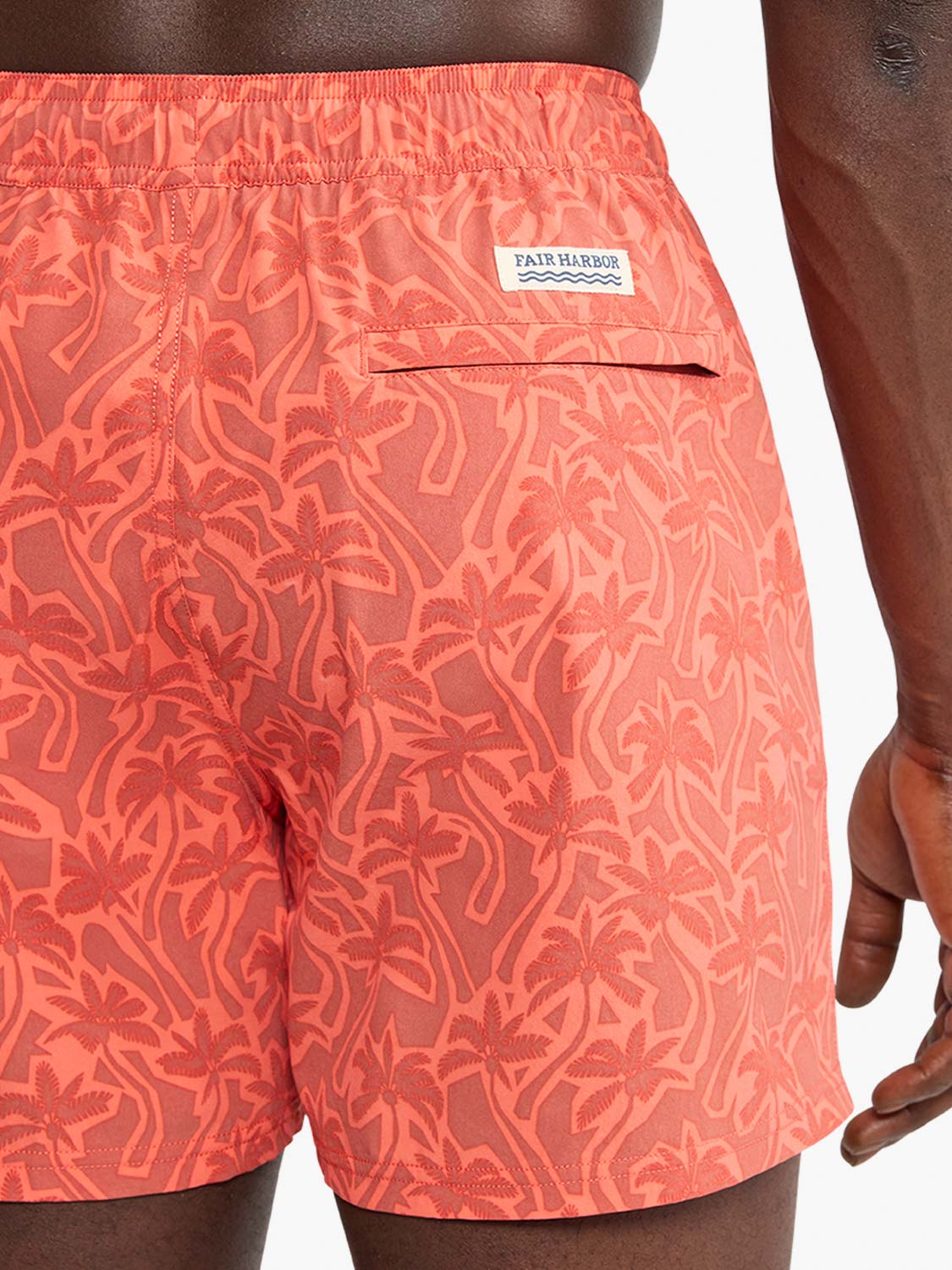 Coral swim trunks with palm tree cutout pattern and Fair Harbor brand label on back pocket.