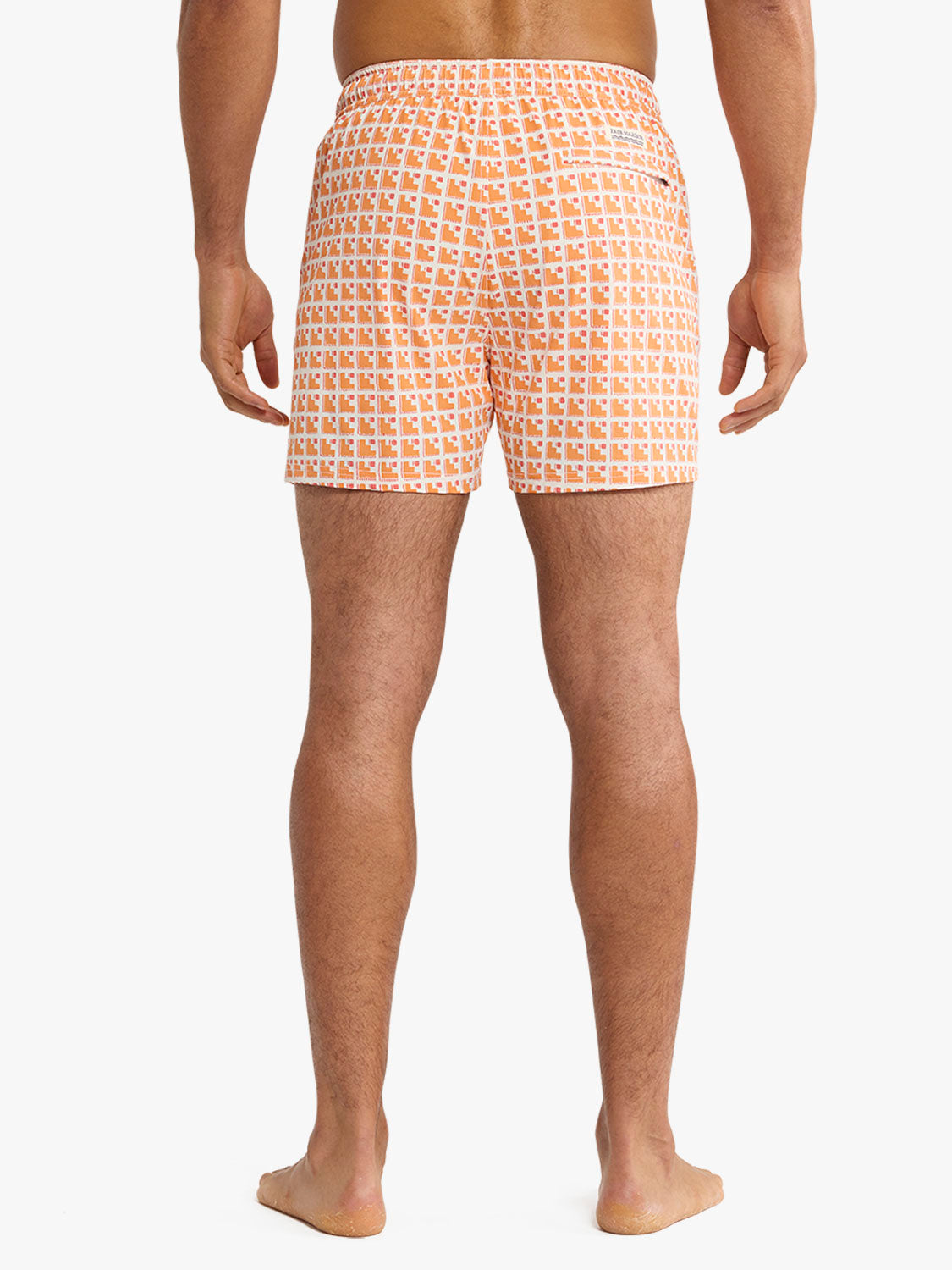 Man wearing orange and white geometric patterned swim shorts viewed from behind.