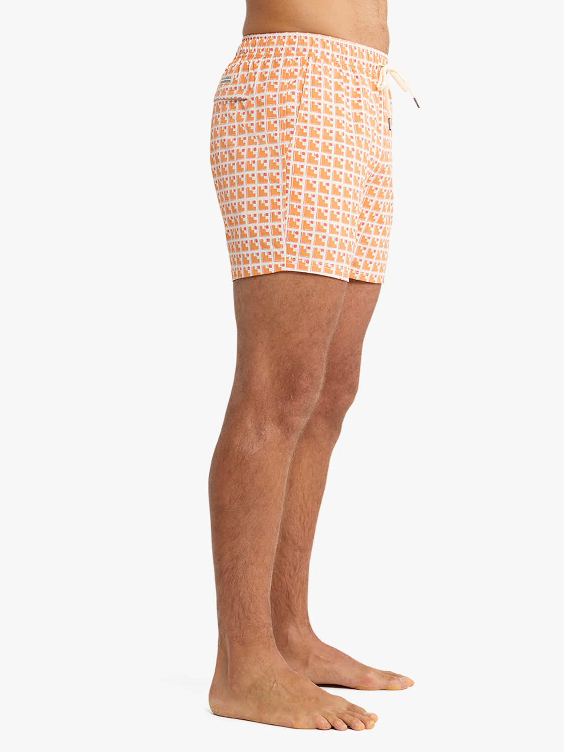 Man wearing orange and white geometric patterned swim trunks with drawstring waistband.