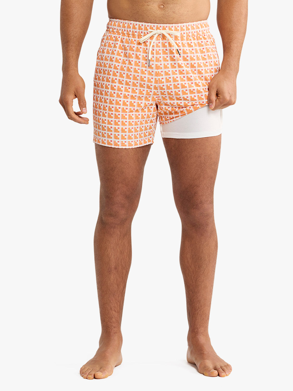 Man wearing orange and white geometric patterned swim trunks with white undershorts and drawstring waist.