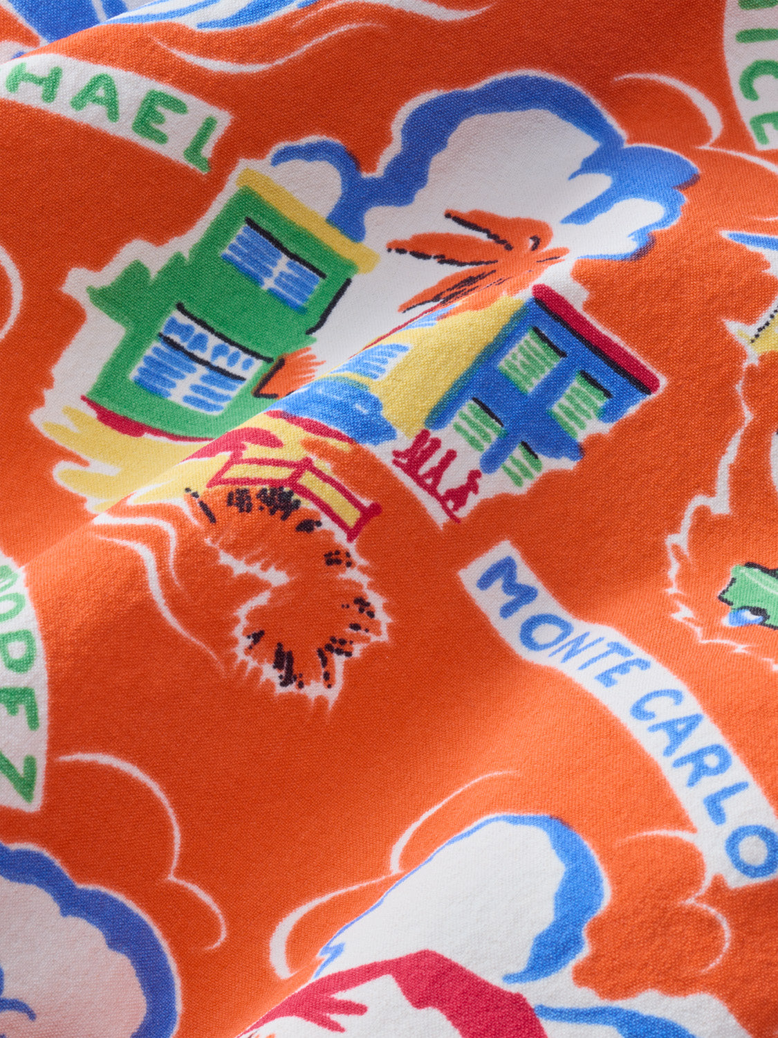 Red fabric featuring colorful illustrated houses, clouds, and decorative text in blue, green, and yellow tones.