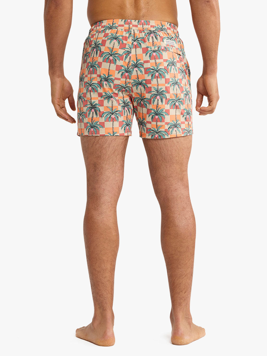 Man wearing swim trunks with checkered pattern and palm tree print in orange and coral.