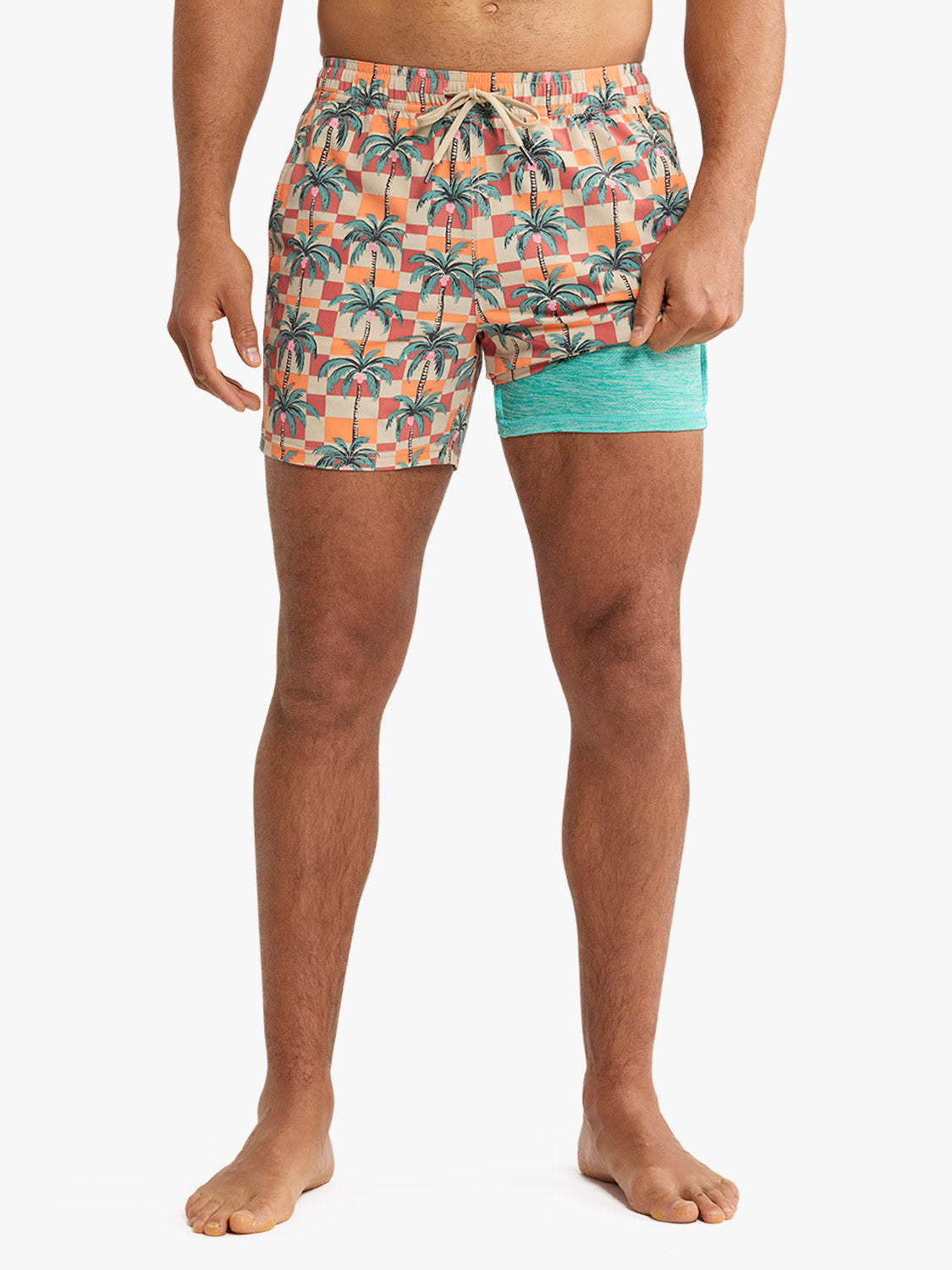 Man wearing orange checkered swim trunk with palm tree print and turquoise liner.