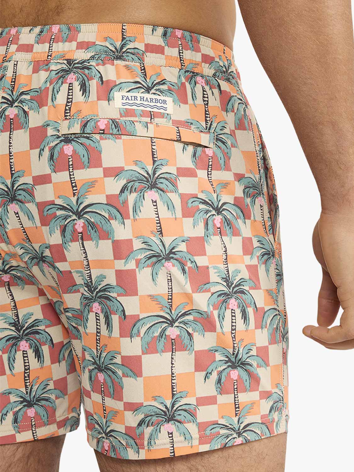 Men's swim shorts featuring a checkered pattern in orange, red, and cream with palm tree print throughout.