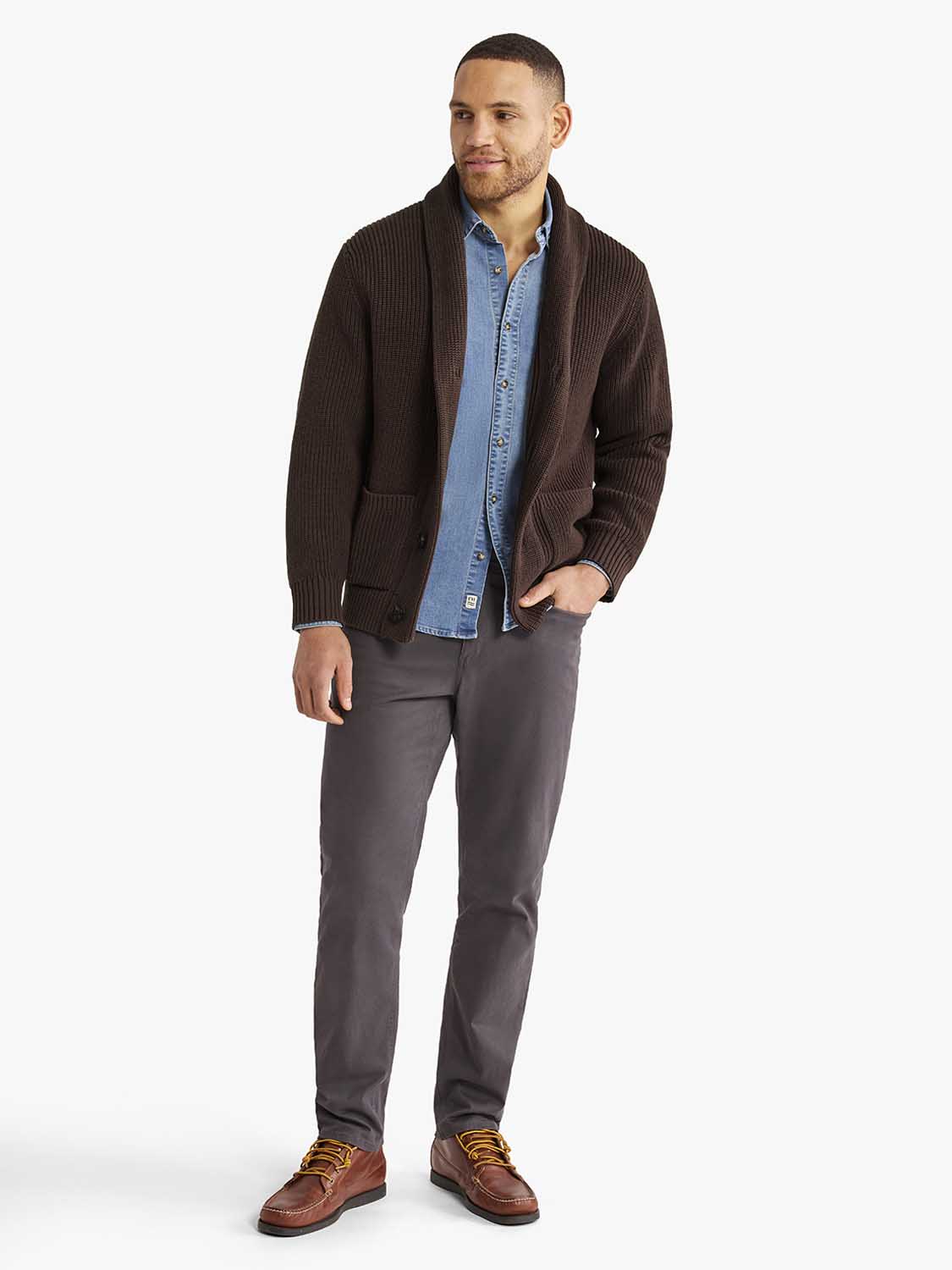 Man wearing a dark brown ribbed cardigan sweater over a blue denim shirt and gray pants.