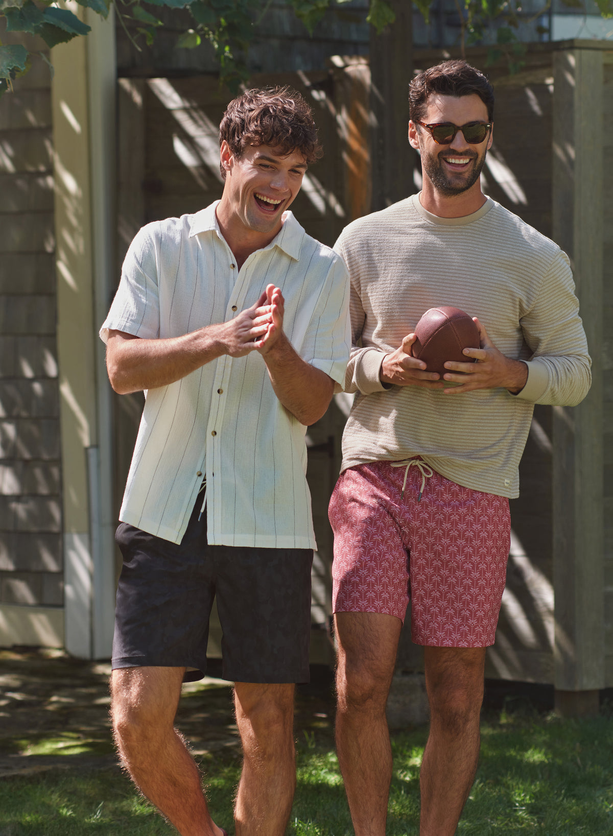 Two men stand outdoors wearing casual summer clothing, with one holding a redstone sand dollar colored trunk.
