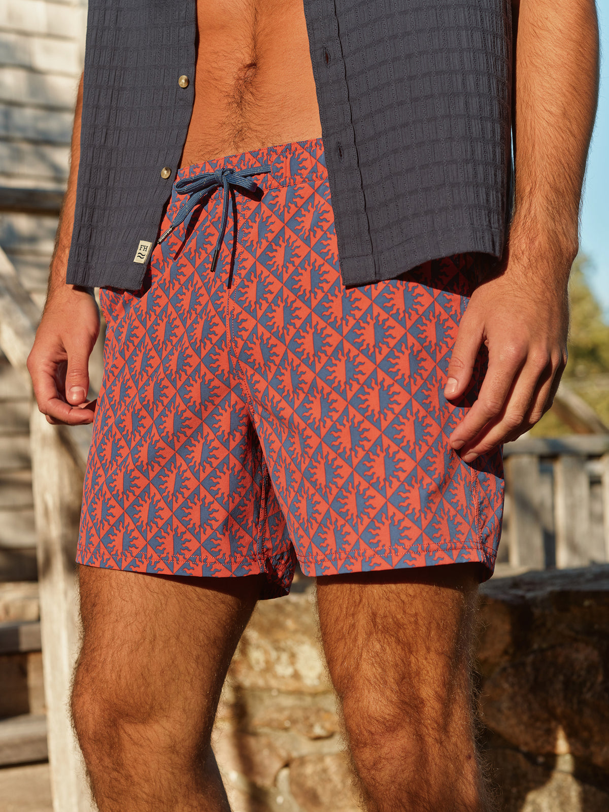 Man wearing red and blue palm-patterned swim trunks with drawstring and dark shirt.