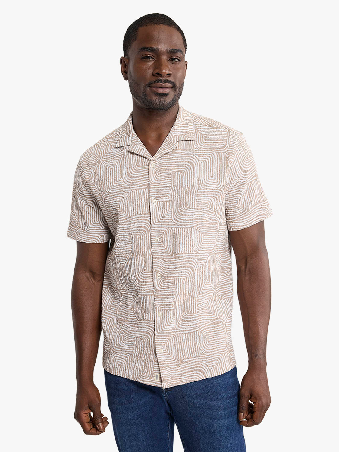Man wearing short-sleeved camp shirt with wavy geometric pattern in tan and cream tones.