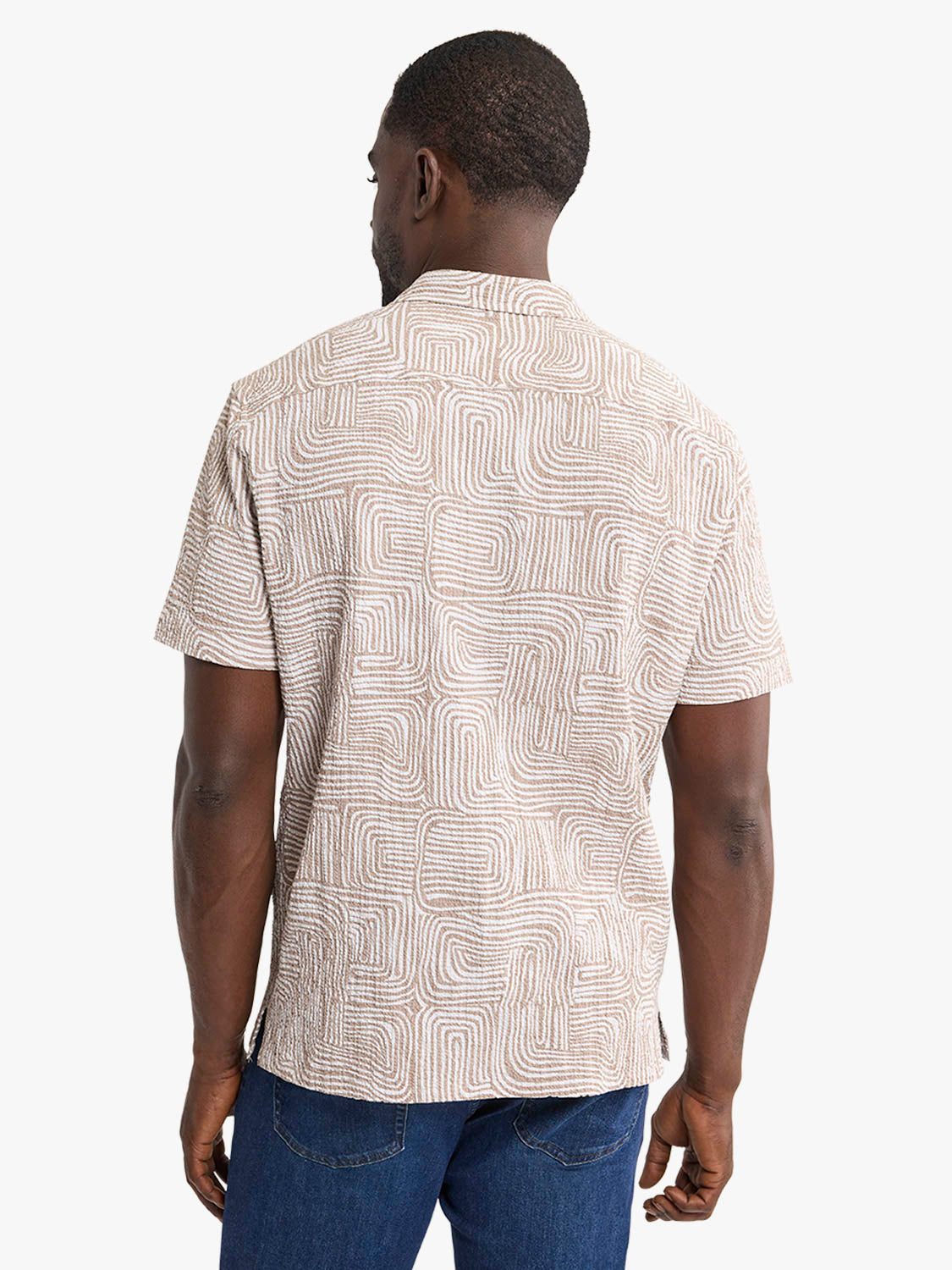 Man wearing a short-sleeved camp shirt with a beige and cream wavy geometric pattern, viewed from behind.