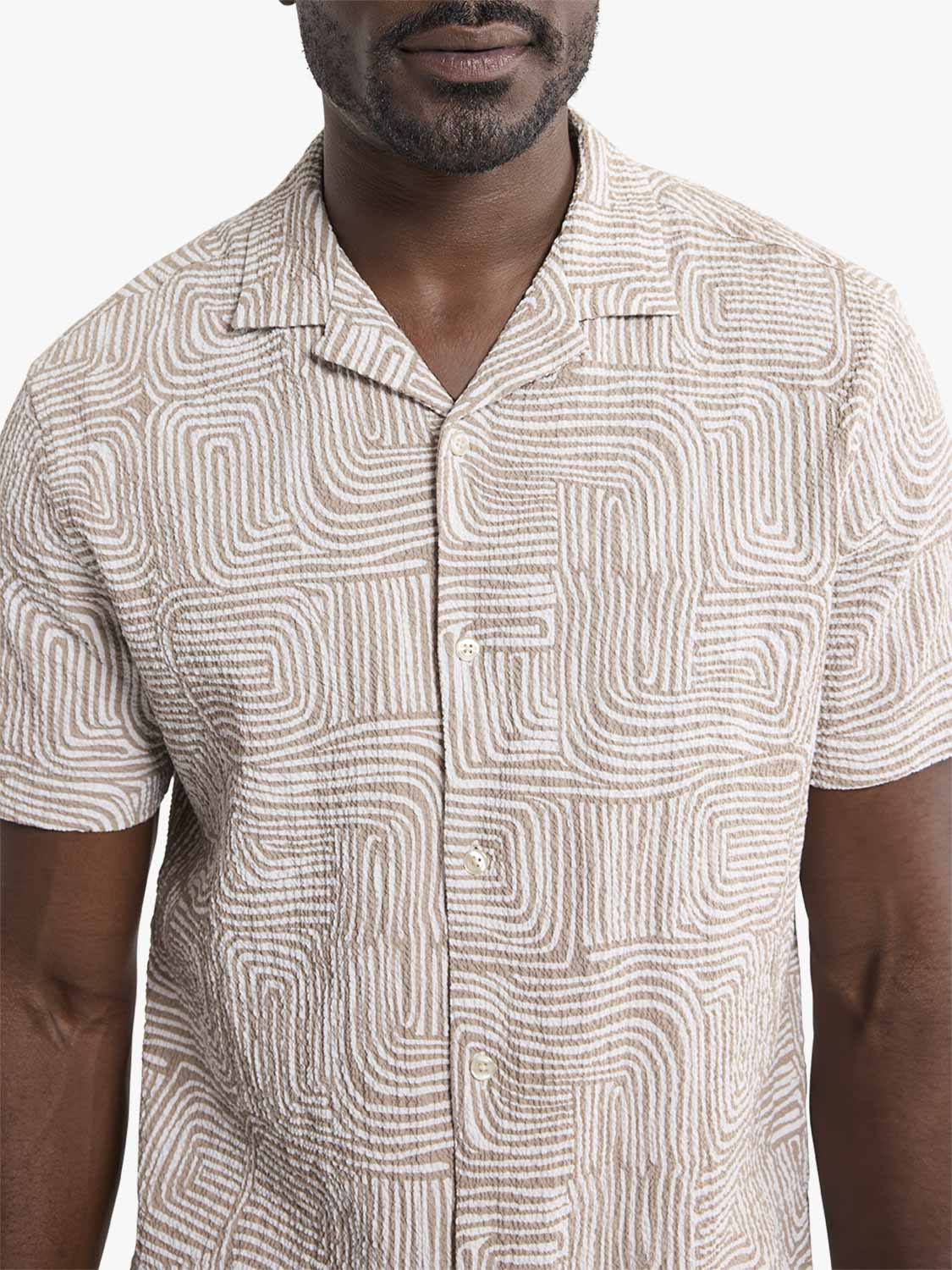 Man wearing a short-sleeved camp shirt with a textured wavy sand-colored geometric pattern.