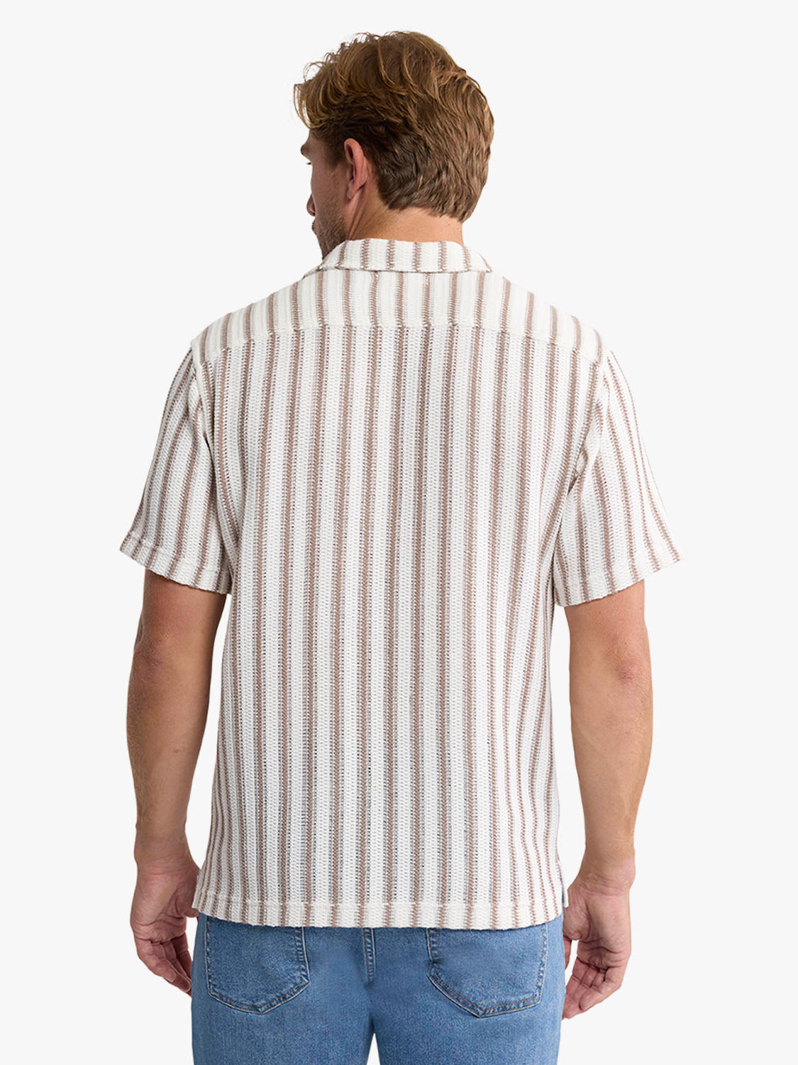 Man wearing a short-sleeved crochet shirt with vertical beige and white stripes, paired with blue jeans.