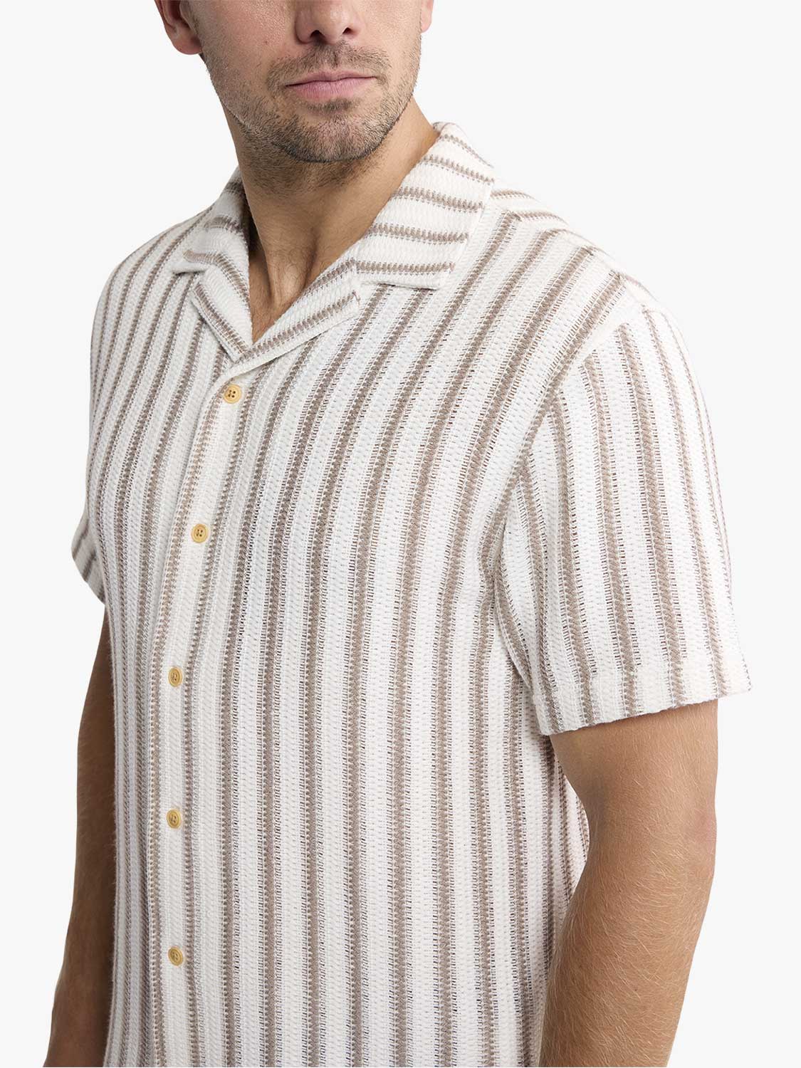 Man wearing a cream and beige striped short-sleeve crochet shirt with gold buttons.