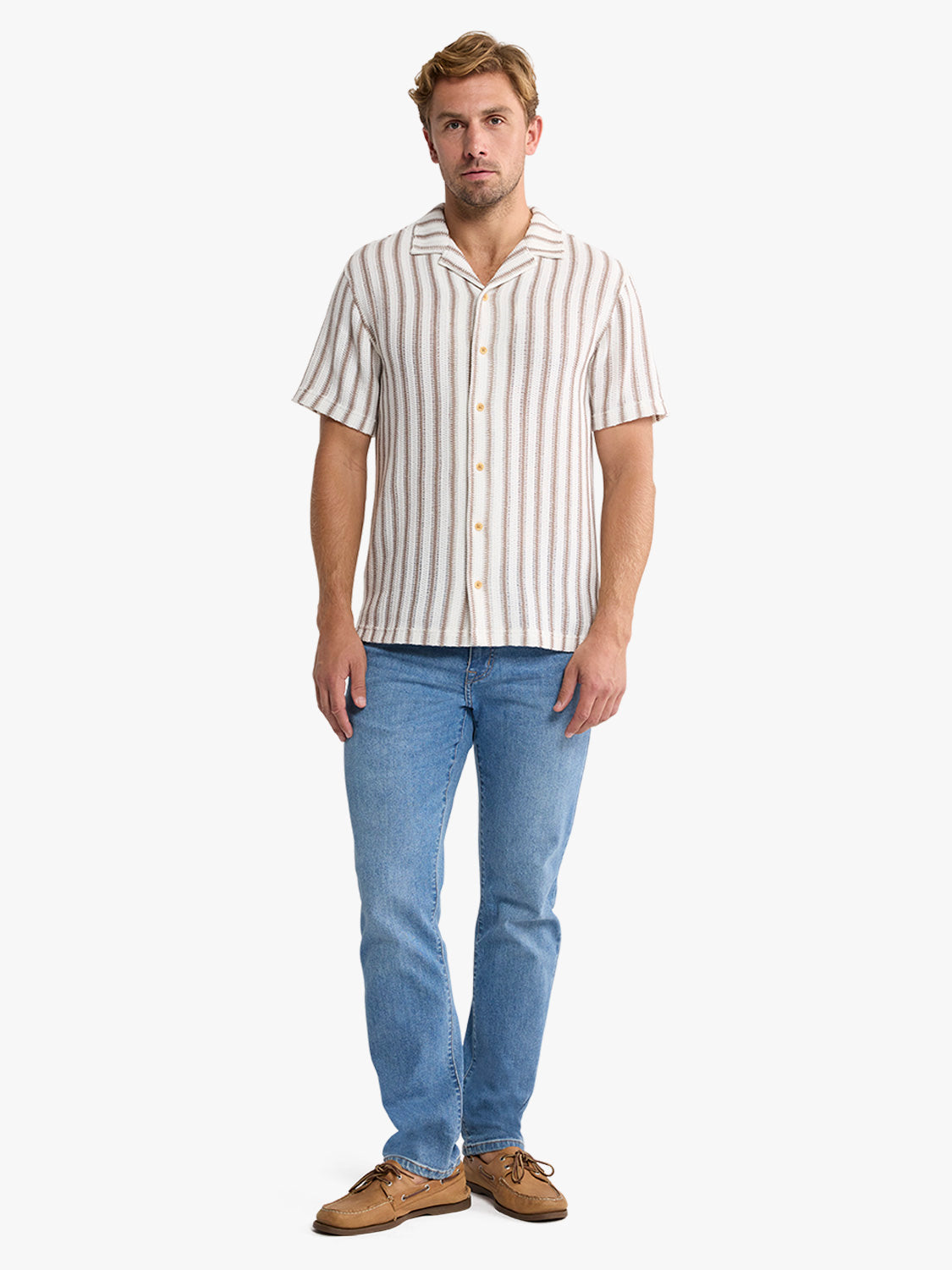 Man wearing a cream and taupe striped short-sleeve button-up crochet shirt with blue jeans.