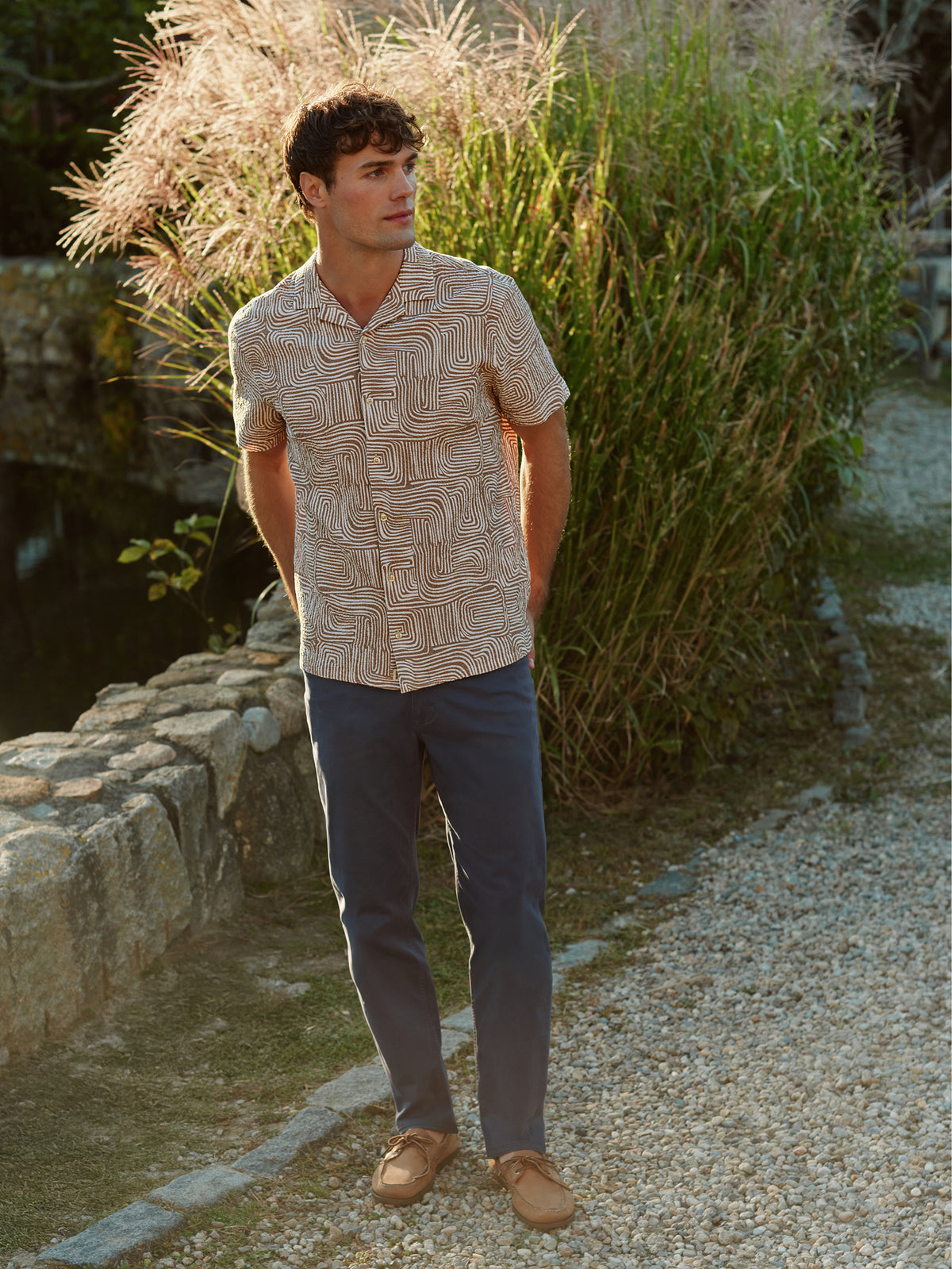 Man wearing a beige textured camp shirt with abstract wavy pattern and navy pants.