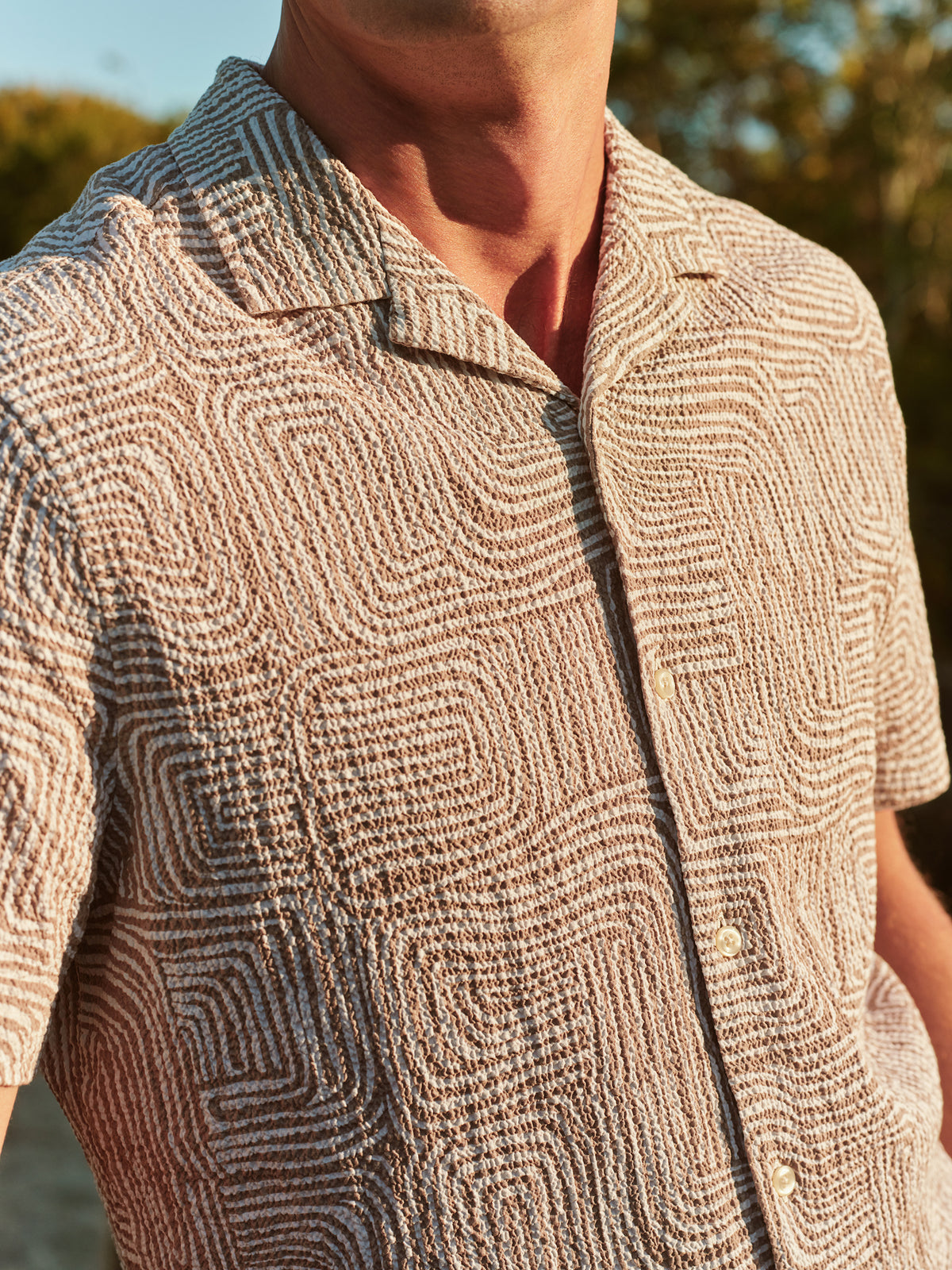 Man wearing a tan and blue textured camp shirt with wavy geometric pattern and short sleeves.