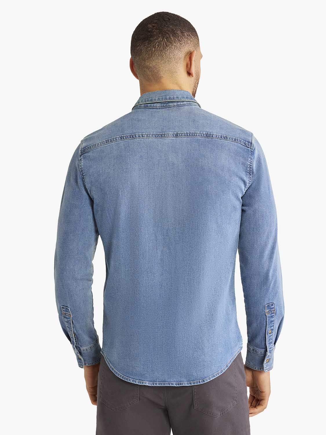 Man wearing a medium blue denim shirt with long sleeves and button front closure.
