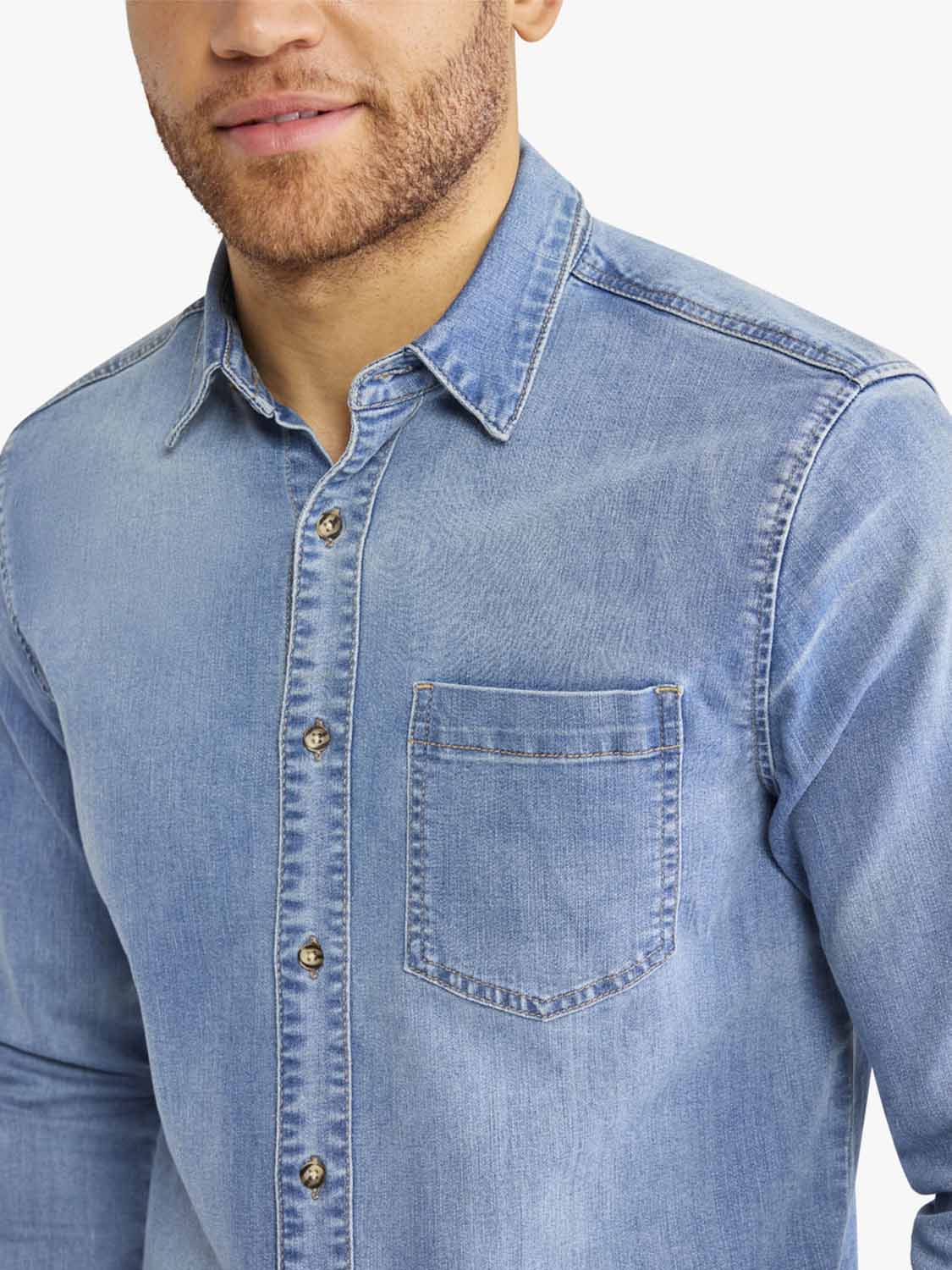 Man wearing a medium-wash denim shirt with a chest pocket and button-front closure.