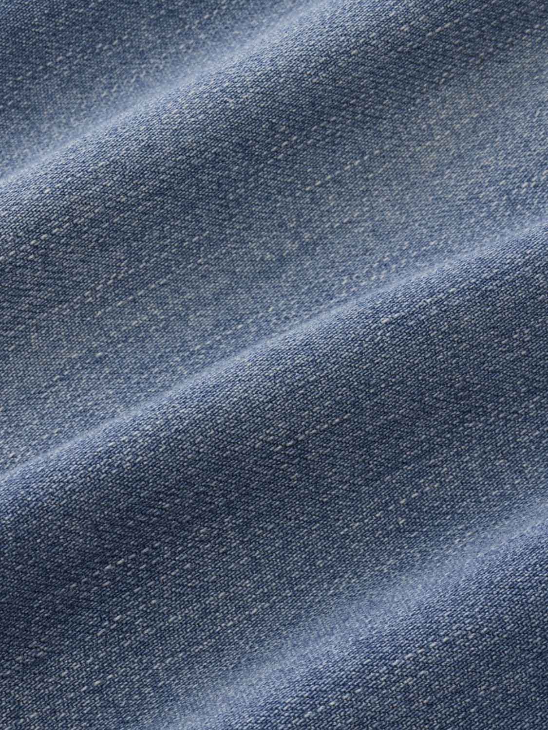 Close-up of medium denim wash fabric showing woven texture and diagonal folds in blue.