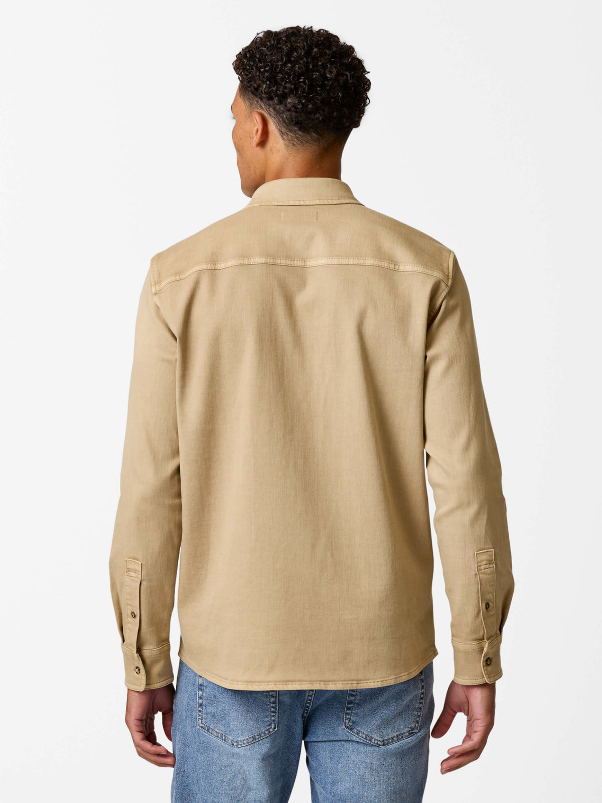 Man wearing a khaki denim shirt with long sleeves and button cuffs, shown from the back.