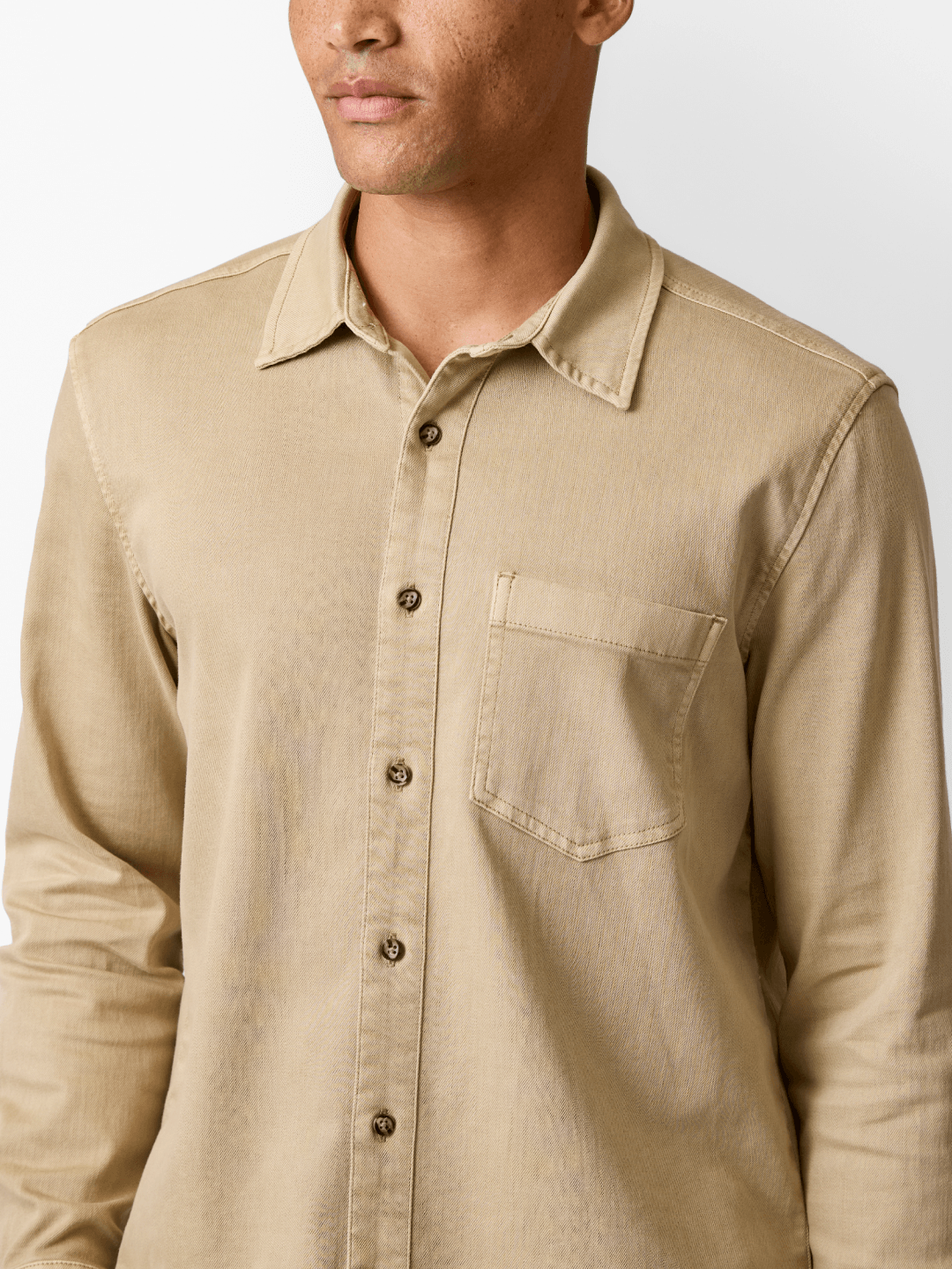 Man wearing a khaki button-up denim shirt with a chest pocket and long sleeves.