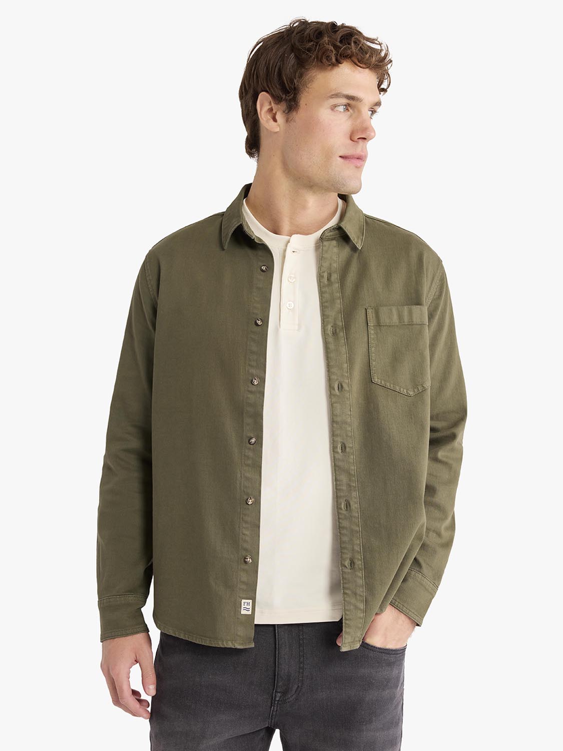 Man wearing an olive-toned denim shirt with a chest pocket over a cream-colored t-shirt.