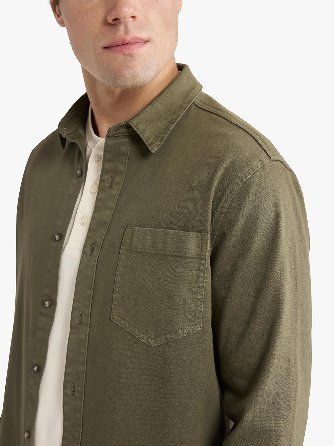 Man wearing an olive-toned denim shirt with a chest pocket over a white shirt.