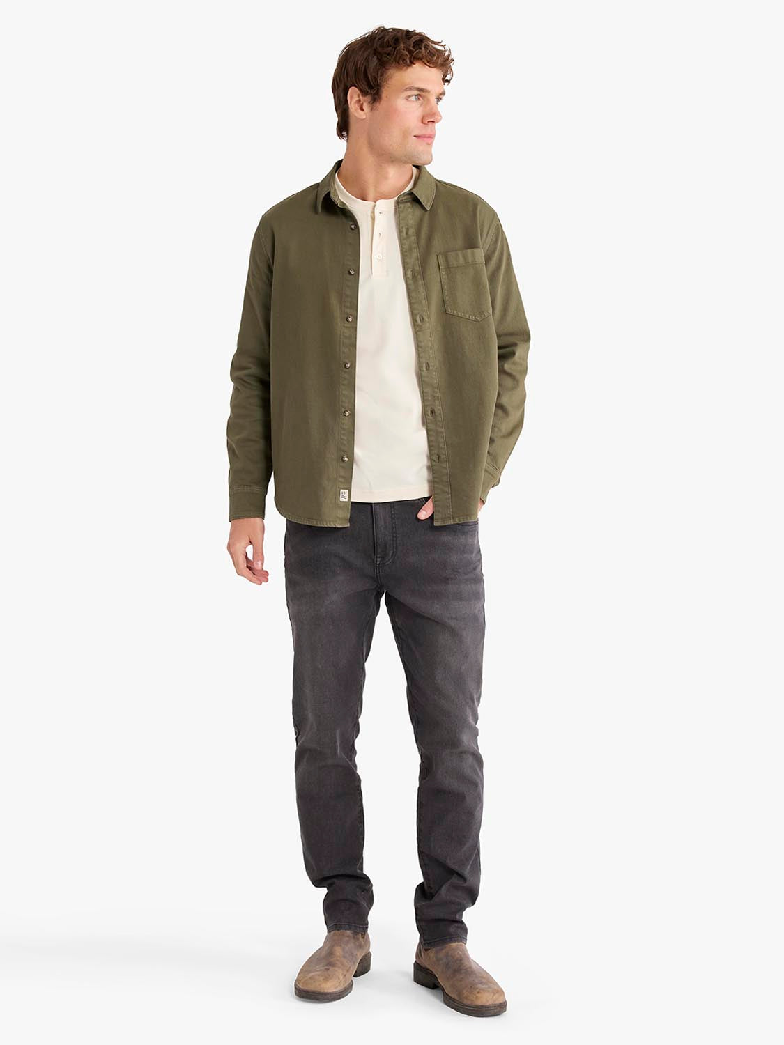 Man wearing olive overdyed denim shirt over white tee with dark jeans and brown boots.