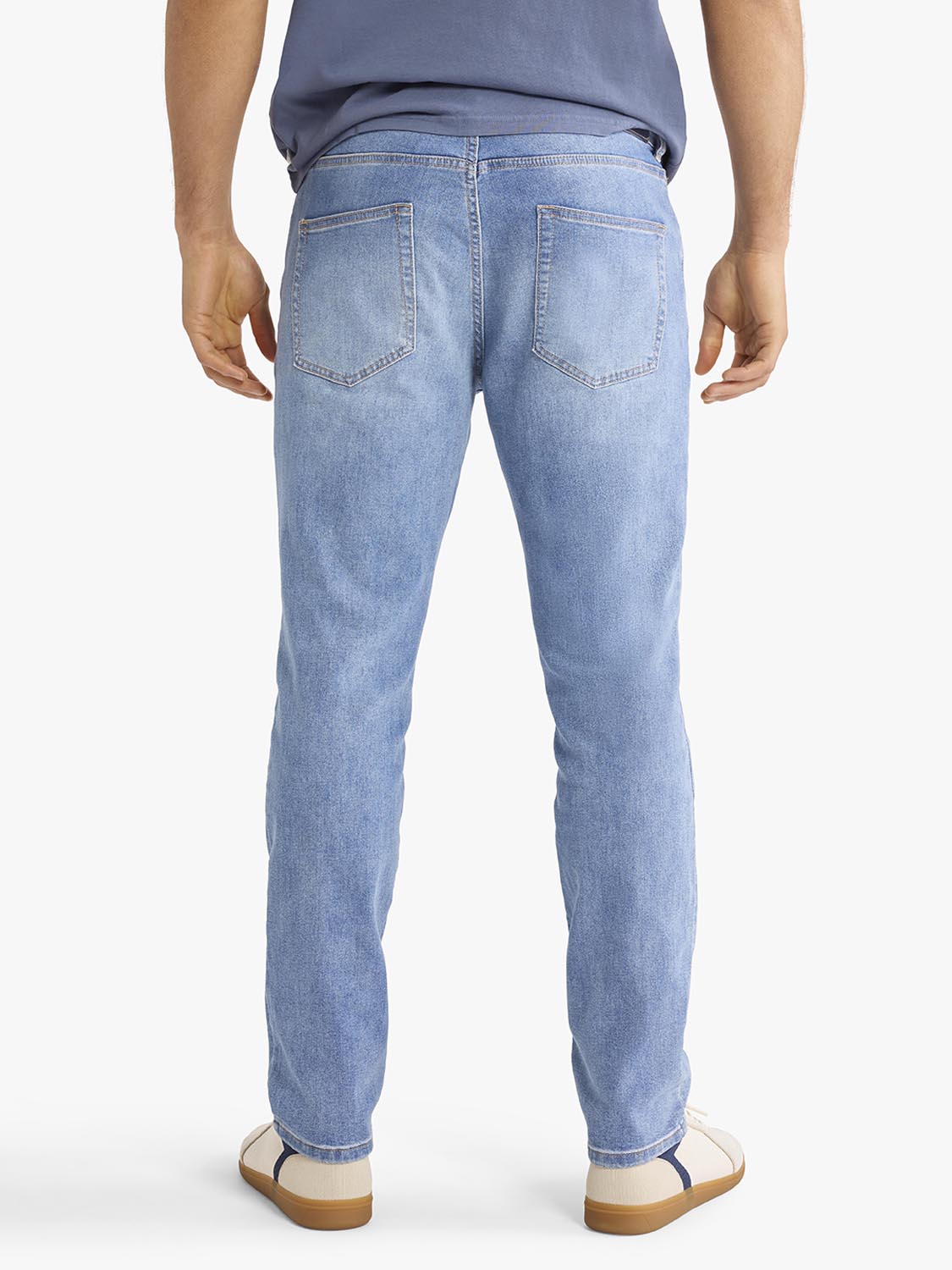 Man wearing light blue denim pants with faded wash and back pockets visible from behind.