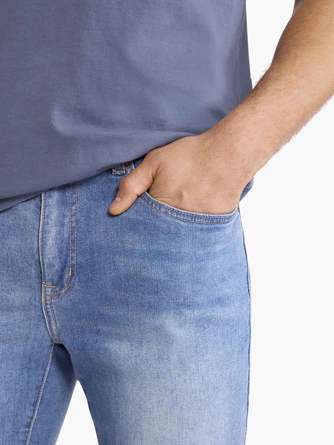 Man wearing light blue stretch denim pants with hand in front pocket and gray shirt visible.