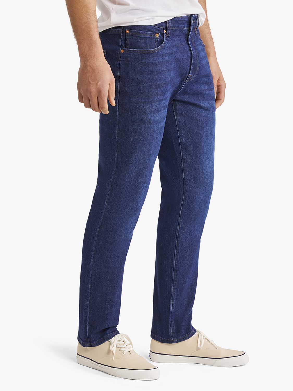 Man wearing dark blue denim pants with copper rivets and beige canvas sneakers.