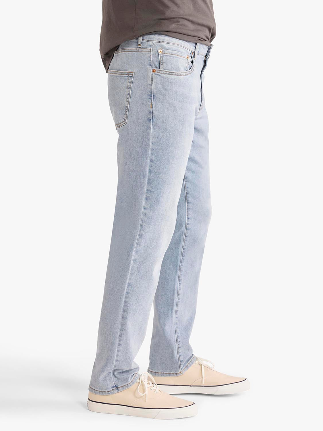 Person wearing light wash denim pants with a straight leg and cream canvas shoes.