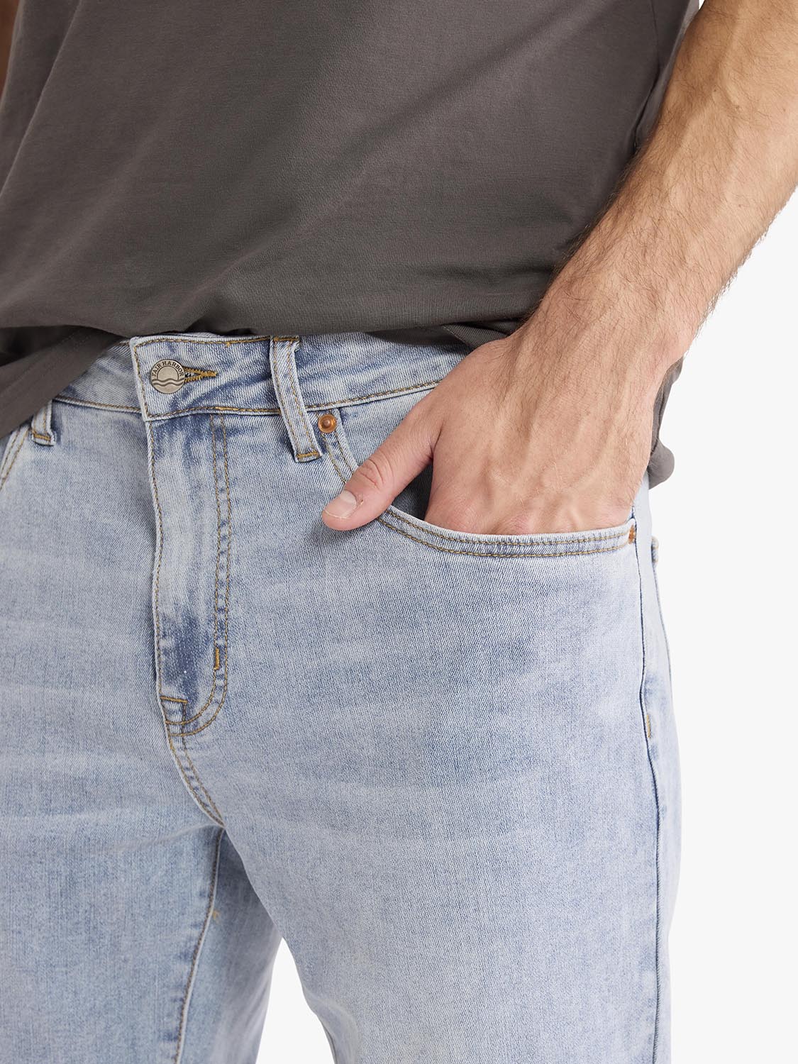 Man wearing light wash denim pants with a gray shirt, showing front pocket and waistband detail.