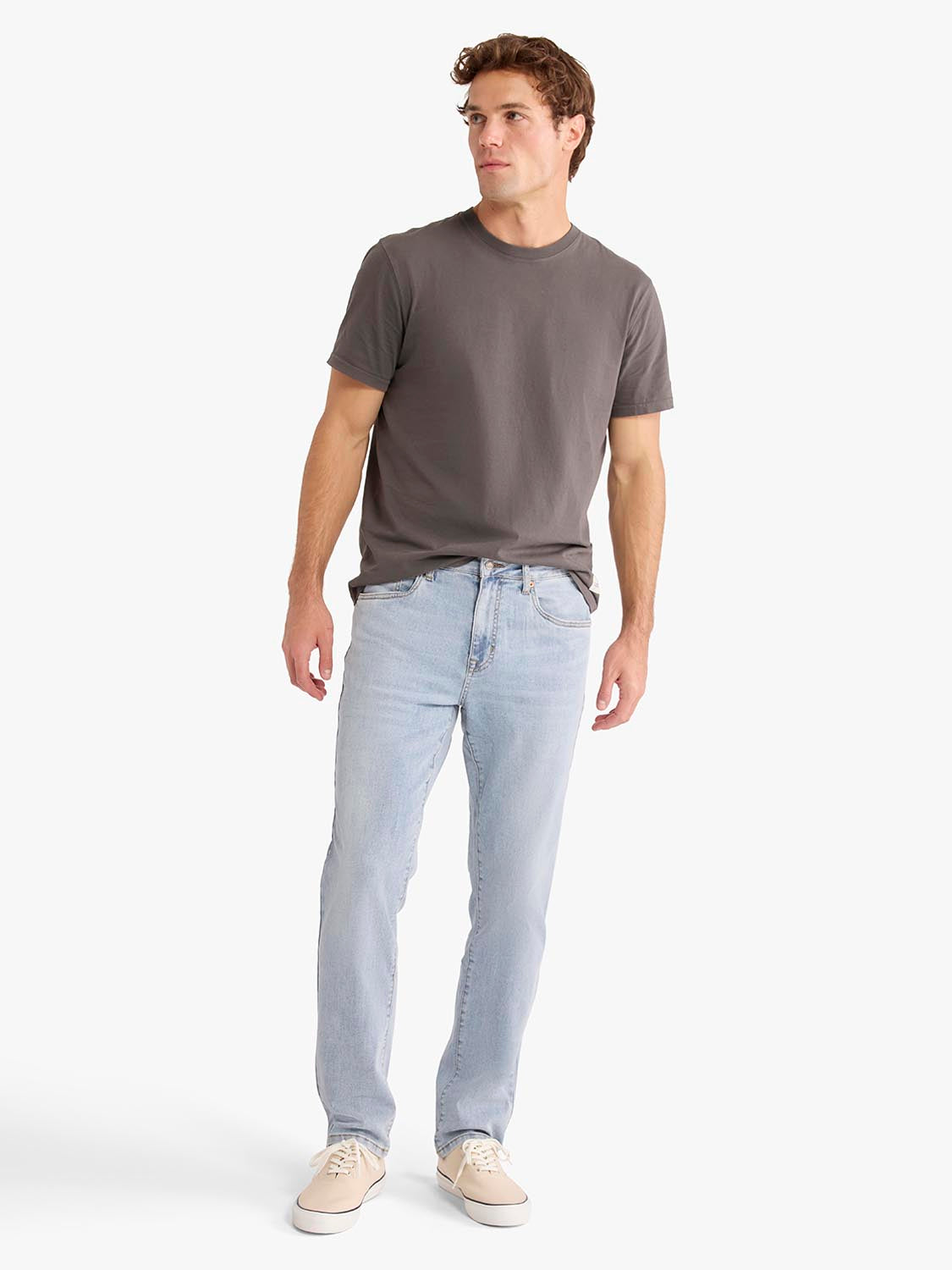 Man wearing light wash denim pants and charcoal gray t-shirt standing against white background.