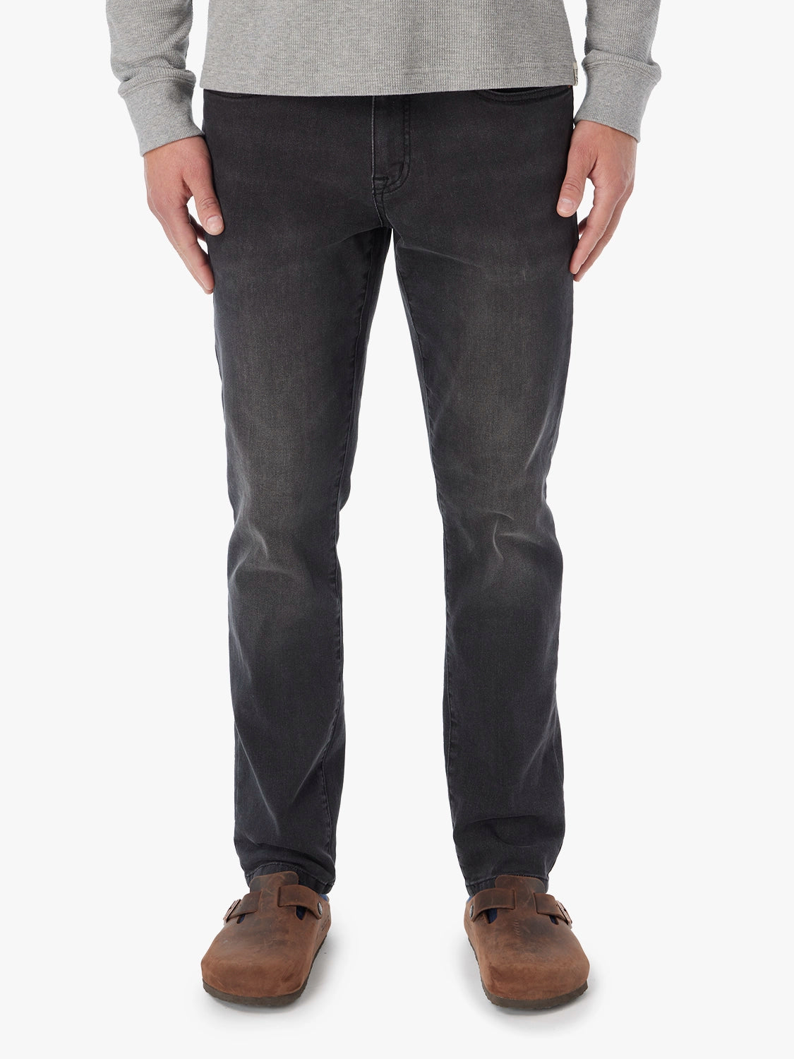Man wearing black wash denim pants with a gray sweater and brown suede shoes.