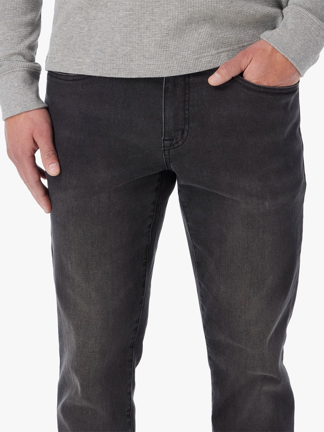 Man wearing black wash denim pants with gray ribbed sweater, hands in pockets.