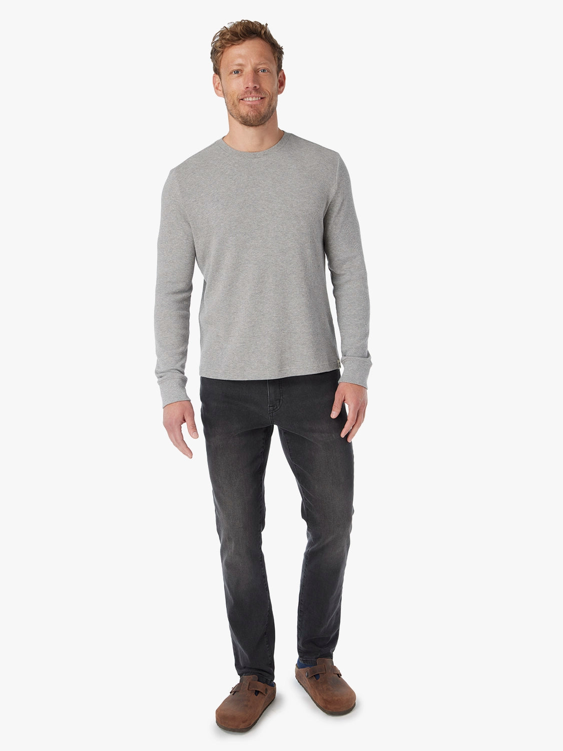 Man wearing a gray long-sleeve shirt and black wash denim pants with brown shoes.