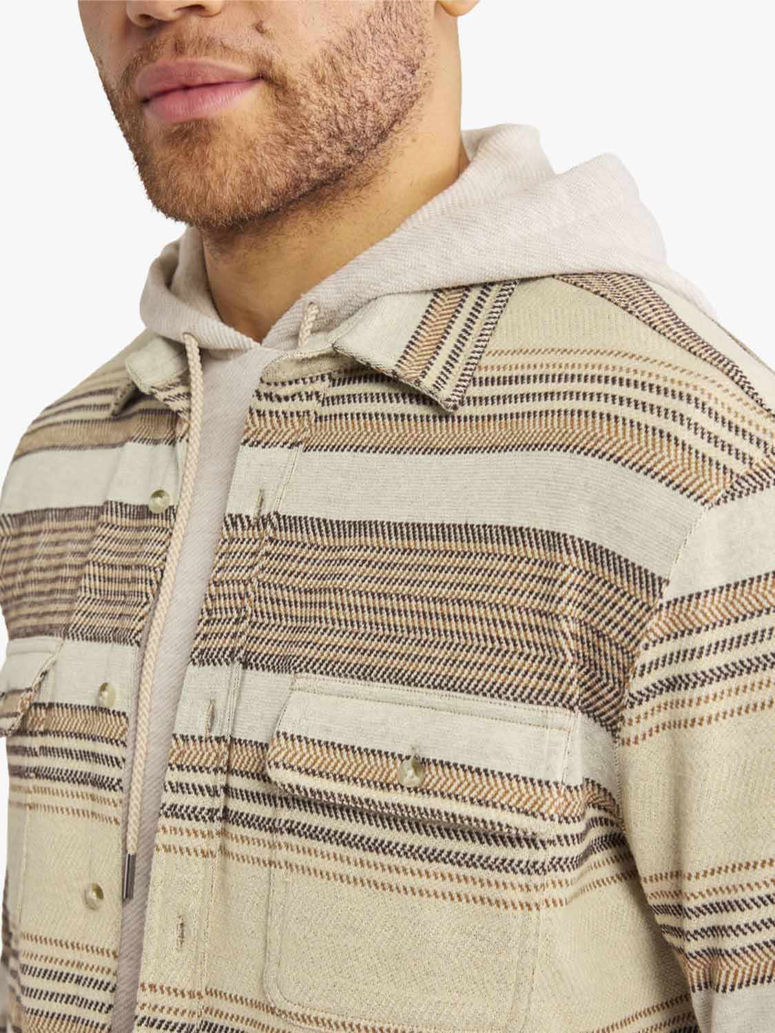 Man wearing a cream-colored flannel shirt with brown and tan horizontal striped pattern throughout.