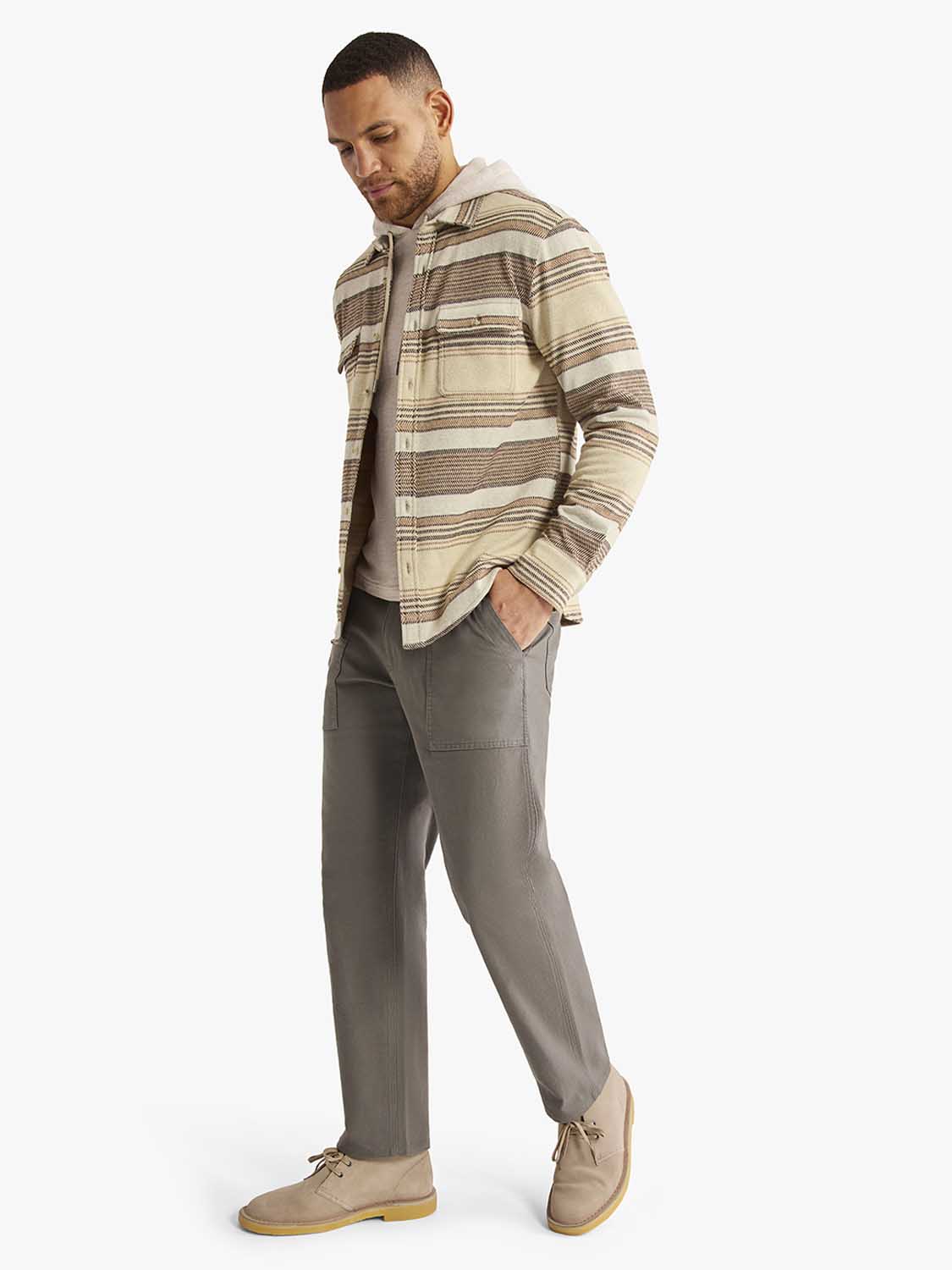 Man wearing a cream and brown striped flannel shirt with gray pants and tan boots.