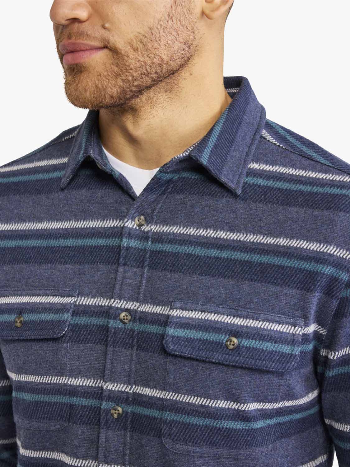 Man wearing navy flannel shirt with horizontal teal and white stripe pattern and button front closure.