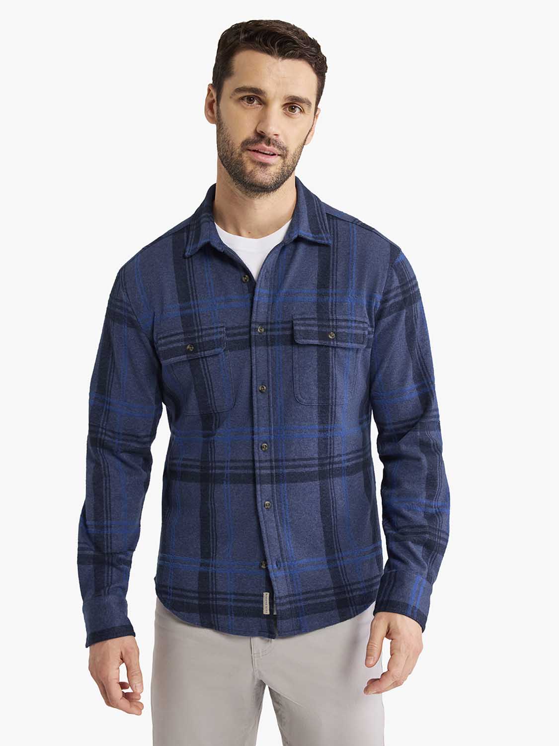 Man wearing navy and blue plaid flannel shirt with button front and chest pockets over white undershirt.
